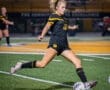 A high school soccer player dribbles the ball during a night match on a vibrant green field. Excitement fills the air.