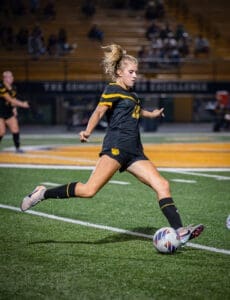 A high school soccer player dribbles the ball during a night match on a vibrant green field. Excitement fills the air.