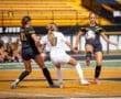 Players compete in a soccer match, with one player passing the ball while others defend in vibrant team uniforms.