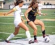 Two female soccer players compete for the ball on the field, showcasing athleticism and teamwork during a match.