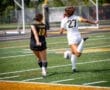 Two female soccer players chase the ball on the field, one in black with “Tigers” and the other in white.