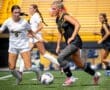 Two female soccer players compete for the ball on a sunny field, showcasing dynamic athleticism and teamwork.