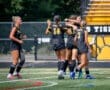 Excited soccer players celebrating a goal on the field, wearing black jerseys and striking poses with joy.