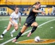 High school soccer players in action, one dribbling the ball while another pursues on a sunny field.