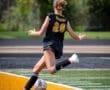 A soccer player in a black jersey kicks a ball during a game, showcasing athleticism on the field.