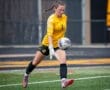 Goalkeeper in yellow uniform catches soccer ball on the field, showcasing athleticism and focus during a game.