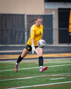 Goalkeeper in yellow uniform catches soccer ball on the field, showcasing athleticism and focus during a game.