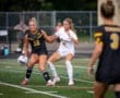 Two female soccer players compete for the ball on the field during a match, showcasing athleticism and teamwork.