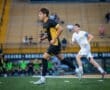 High school soccer player in action during a competitive match, wearing a black and yellow uniform on a field.