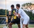 Two soccer players compete for the ball, showcasing intense action during a match on the field at sunset.