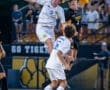 Two soccer players compete for a header while another player anticipates the play in an energetic match.