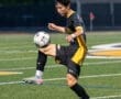 Youth soccer player skillfully juggling a ball on a field during a nighttime match, showcasing athleticism and focus.