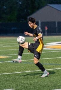 Youth soccer player skillfully juggling a ball on a field during a nighttime match, showcasing athleticism and focus.