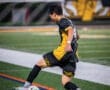Soccer player in a black and yellow jersey skillfully preparing to kick a ball on a vibrant field at night.