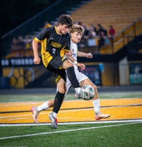 High school soccer players compete for the ball under stadium lights during an intense match, showcasing athleticism.