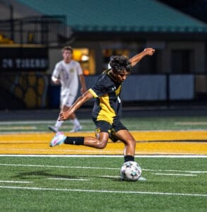 Soccer player in a black and yellow uniform strikes a ball on the field during a night game.