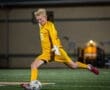 Goalkeeper in yellow kit making a save during a night soccer match on the field.