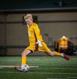 Goalkeeper in yellow kit making a save during a night soccer match on the field.