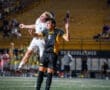 High school soccer players competing for the ball in mid-air at Newman Stadium during an evening match.