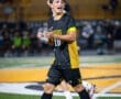 Soccer player in black and yellow uniform passionately gesturing during an evening match on the field.