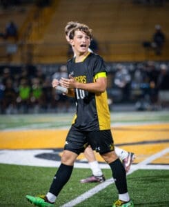 Soccer player in black and yellow uniform passionately gesturing during an evening match on the field.