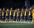 Soccer team standing in formation on the field, showing teamwork and sportsmanship before a match.