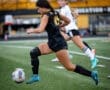 A female soccer player dribbles the ball on the field during a game, showcasing athleticism and team spirit.