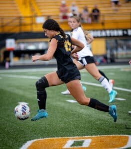 A female soccer player dribbles the ball on the field during a game, showcasing athleticism and team spirit.
