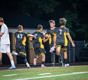 Soccer players celebrating a goal under stadium lights, showcasing teamwork and excitement during a night game.