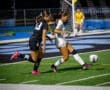 Two female soccer players compete for the ball on a well-lit field during a night game, showcasing athleticism and teamwork.