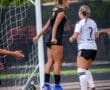 Two female soccer players celebrate a goal near the net, showcasing athleticism and team spirit during a game.