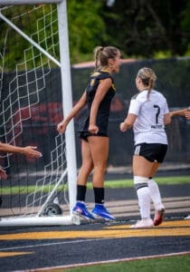 Two female soccer players celebrate a goal near the net, showcasing athleticism and team spirit during a game.