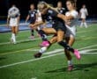Two female soccer players compete for the ball during a night game, showcasing athleticism on a vibrant field.