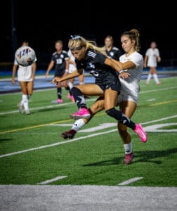 Two female soccer players compete for the ball during a night game, showcasing athleticism on a vibrant field.