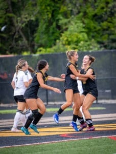Girls' soccer team celebrating a goal on the field, showcasing excitement and teamwork during a match.