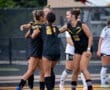 Team members celebrate a goal on the soccer field, showcasing teamwork and excitement in athletic wear.