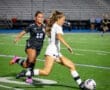Two soccer players competing for the ball on a night field, showcasing athleticism and teamwork in action.