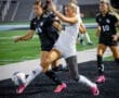 Two female soccer players compete for the ball on a field, showcasing skill and athleticism during a night game.