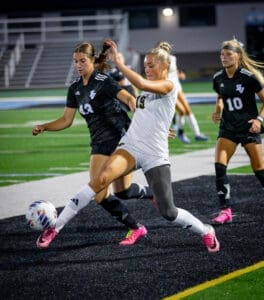 Two female soccer players compete for the ball on a field, showcasing skill and athleticism during a night game.