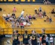 High school soccer team huddles on the field with fans in the stadium cheering in the background. Team colors are black and yellow.