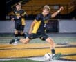 High school soccer player with jersey number 3 kicks a ball during a night game on a turf field.
