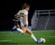 Player number 22 from the Tigers soccer team kicks the ball during a night game on a synthetic field.