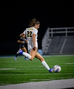 Player number 22 from the Tigers soccer team kicks the ball during a night game on a synthetic field.