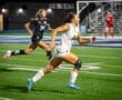 Two female soccer players sprinting on a field at night, showcasing athleticism and competition during a game.