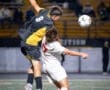High school soccer players leap for the ball in a competitive match under stadium lights.
