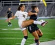 Two female soccer players collide on the field during an intense night match, showcasing athleticism and competition.