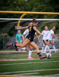A soccer player wearing number 15 kicks the ball during a match, with teammates and opponents in the background.