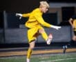 Goalkeeper in yellow uniform leaps into action during a night soccer match, showcasing agility and focus on the field.