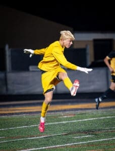 Goalkeeper in yellow uniform leaps into action during a night soccer match, showcasing agility and focus on the field.