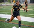 Player in black soccer uniform striking ball on field, showcasing athletic skill during game. Teammates in background.